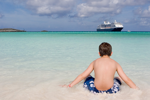 Boy on the beach looking at a cruise ship.