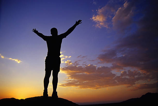 istock silhouette man with arms raised into sunset sky landscape 90642319