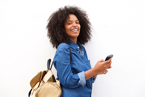Portrait of cheerful black woman with backpack holding mobile phone