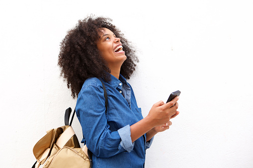 Portrait of laughing black woman with backpack and mobile phone