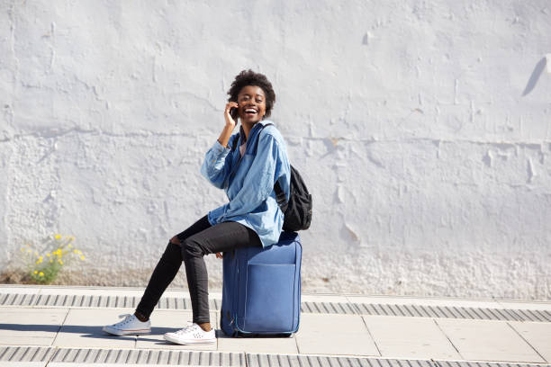 istock Afro american female sitting on suitcase outdoors and talking on mobile phone 906498492