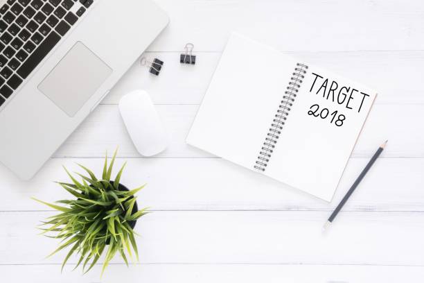 istock Minimal work space - Creative flat lay photo of workspace desk with Target 2018 New Year list notebook and laptop on wooden background. Top view flat lay photography. 2018 happy new year concept. 906509302