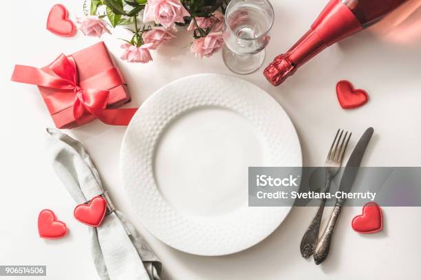 Cena Di San Valentino Con Ambiente Da Tavolo Con Regalo Rosso Bicchiere Per Champagne Una Bottiglia Di Champagne Rose Rosa Ornamenti Per Il Cuore Con Argenteria Su Sfondo Bianco Vista Dallalto Biglietto Di San Valentino - Fotografie stock e altre immagini di San Valentino - Festività pubblica