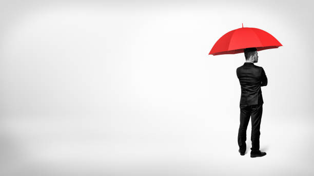 istock A high contrast view on a businessman standing in half-turn under an open red umbrella 906569894