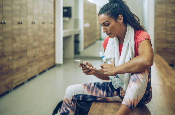istock Young athletic woman sitting on a bench in dressing room and using smart phone. 906597332