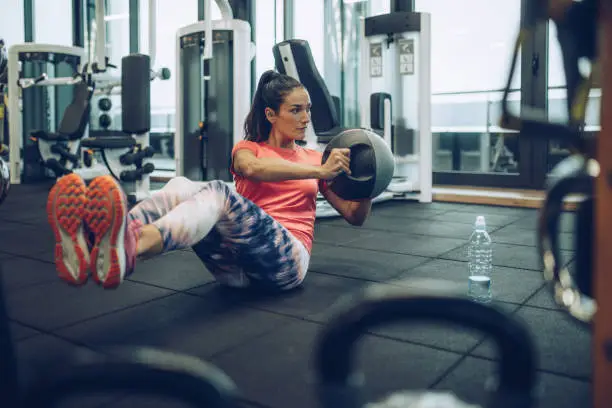 Young female athlete doing sit-ups with medicine ball in a gym.