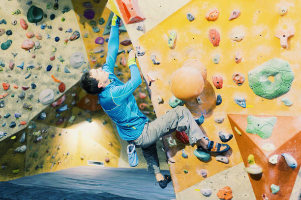 istock Young man practicing rock-climbing on a rock wall indoors. 906602576