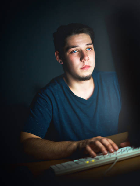 istock Young man sits in the dark staring at computer monitor 906603046