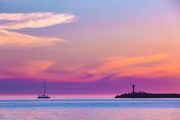 Coastal seascape on the Black Sea, Sochi, Russia. Summer colorful pink purple sunset with graceful clouds and a silhouette of a sailing boat with a descending sail next to the lighthouse on the beach. sochi photos stock pictures, royalty-free photos & images