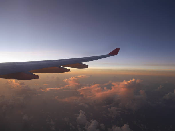 istock Aerial view from airplane, seeing plane's wing and pink sunset light from left side, over clouds horizon under blue sky which is getting dark 906609404