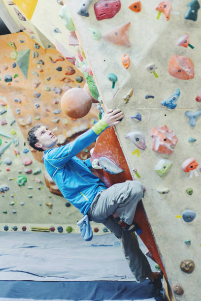 istock Young man practicing rock-climbing on a rock wall indoors. 906612546