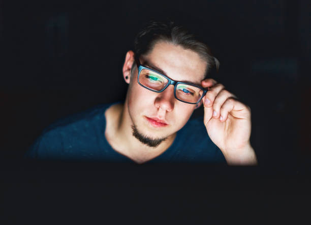 istock Young man sits in the dark staring at computer monitor 906626322