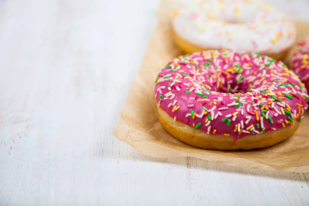 Pink donuts on paper Pink donuts on paper on a wooden background. Delicious dessert. alcorza stock pictures, royalty-free photos & images