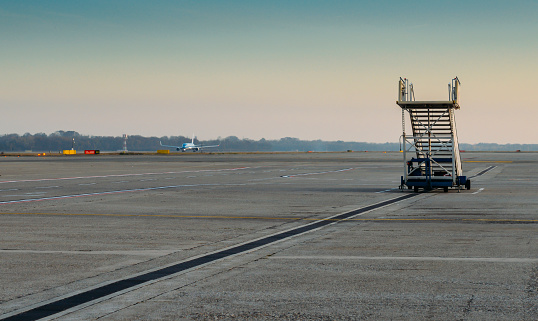 Lone airplane stairs on the tarmac at airport with airplane in background taxiing - solitude theme of missing the flight