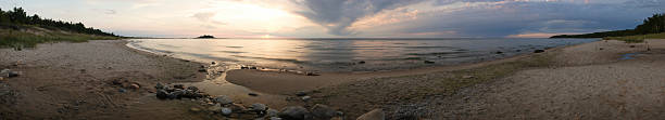 Panorama: Beach at Sunset The setting sun lights an empty beach as receding storm clouds streak the sky. Lake Michigan. Total field of view is approximately 180 degrees. (Stitched from 12 shots with a tripod mounted panoramic head from a Canon 20D at ISO 100, 0.8 second exposure.) lake michigan photos stock pictures, royalty-free photos & images