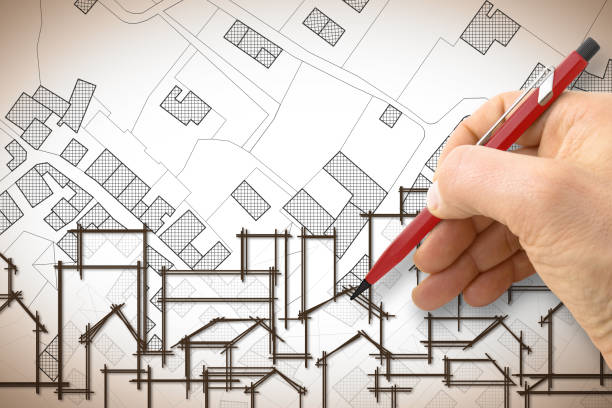 istock Architect drawing a residential building over an imaginary cadastral map of territory with buildings, fields and roads 906643466