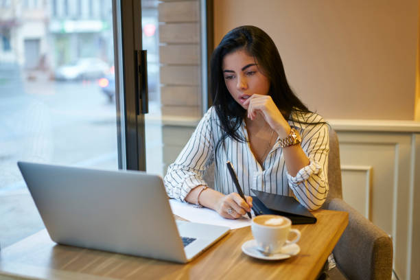 istock Pensive brunette marketing experts making notes while watching video online pondering on creative solutions, young female entrepreneur in stylish wear searching information in network making planings 906658328
