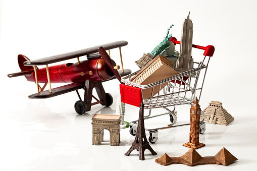 Shopping for a vacation or holiday and travel around the world concept with and vintage airplane and a shopping cart filled and surrounded by souvenirs representing the world most famous landmarks