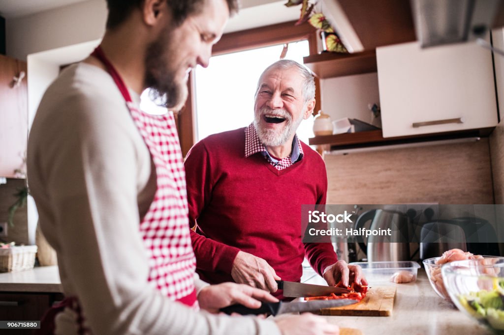 Hipster son with his senior father cooking in the kitchen. Hipster son with his senior father cooking in the kitchen. Two generations indoors. Cooking Stock Photo