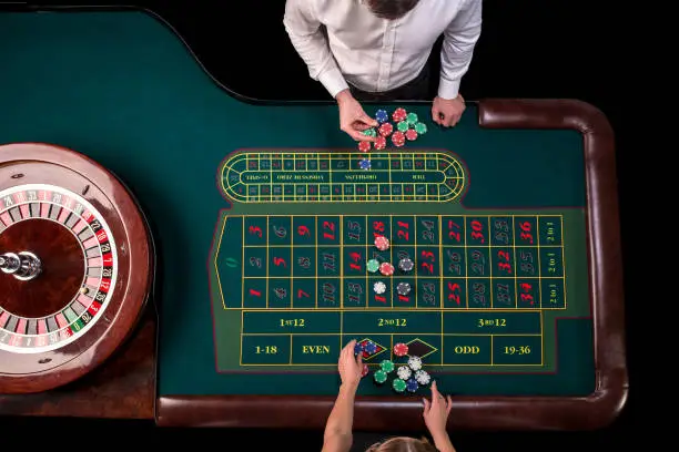 Photo of Man croupier and woman playing roulette at the table in the casino. Top view at a roulette green table with a tape measure