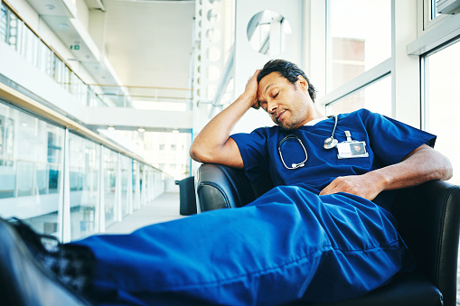 Tired medical professional sitting on chair and sleeping in hospital waiting area