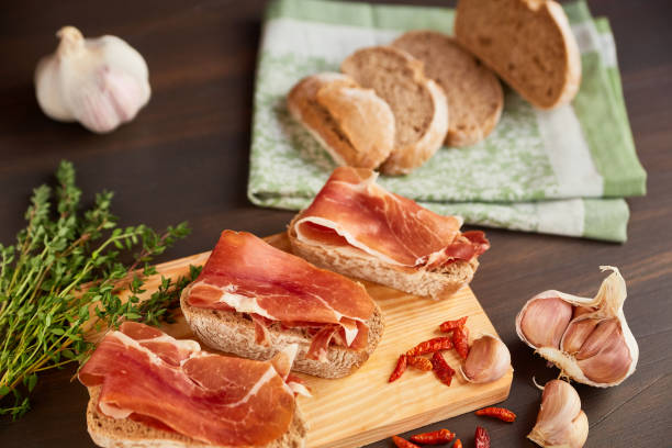 istock Sandwiches made from hand-made rye bread and thin chopped fresh bacon. Fresh green thyme and hot red pepper. Succulend bacon on a wooden board. 906722952