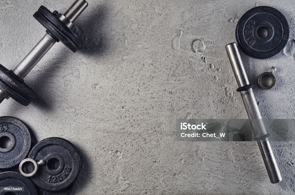 Fitness or bodybuilding background. Dumbbells on gym floor, top view Fitness or bodybuilding concept background. Product photograph of old iron dumbbells on grey, conrete floor in the gym. Photograph taken from above, top view with lots of copy space Gym Stock Photo