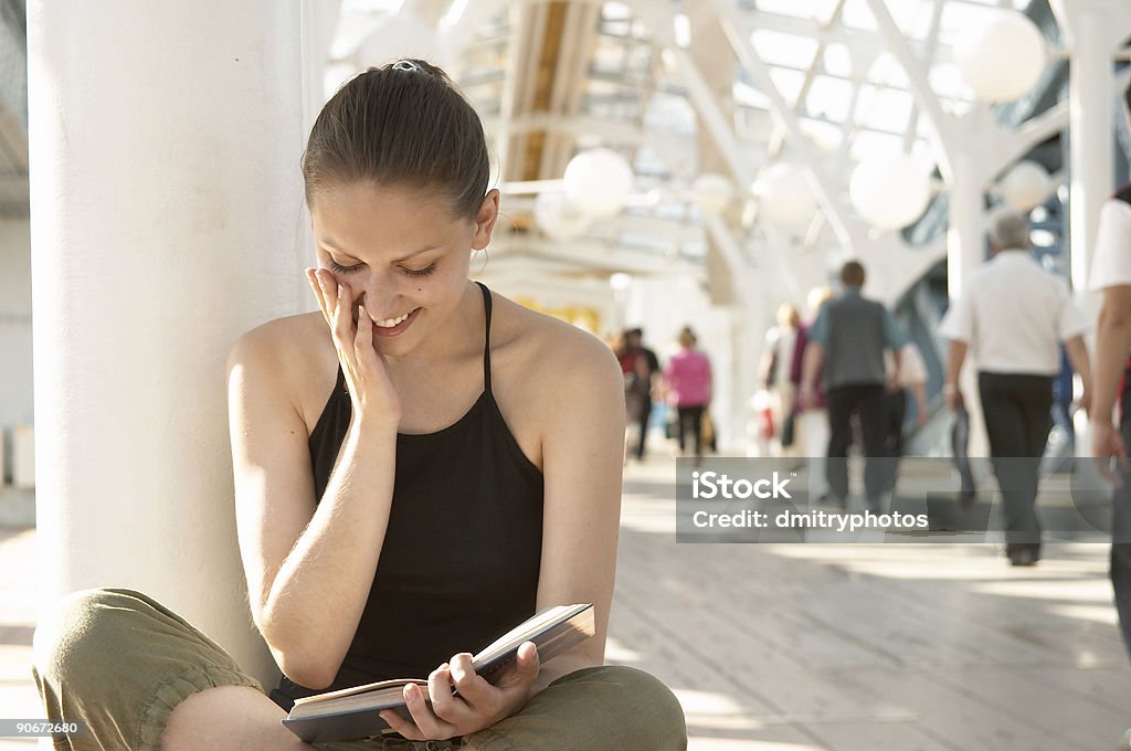 Young woman sitting down reading a book and smiling Reading girl Book Stock Photo