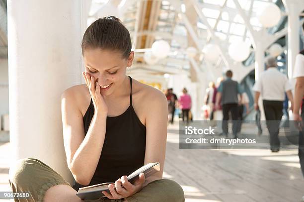 Young Woman Sitting Down Reading A Book And Smiling Stock Photo - Download Image Now