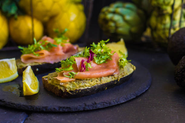istock morning breakfast with hot coffee and a sandwich with avocado, soft cheese, lemon and red fish trout on a dark background 906727254