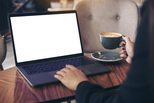 istock Mockup image of a businesswoman using laptop with blank white desktop screen while drinking hot coffee on wooden table in cafe 906738056