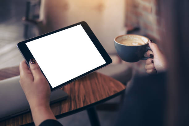 immagine beffarda delle mani della donna che tiene il tablet pc nero con schermo bianco e tazza di caffè sullo sfondo del caffè - pc desktop pc women desk foto e immagini stock