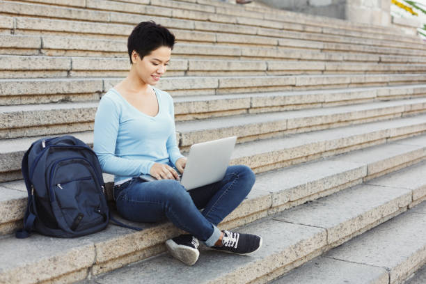 istock Smiling woman sitting on stairs using laptop 906740106