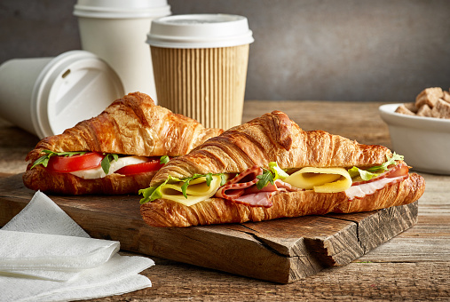 croissant sandwiches and coffee cups on wooden table