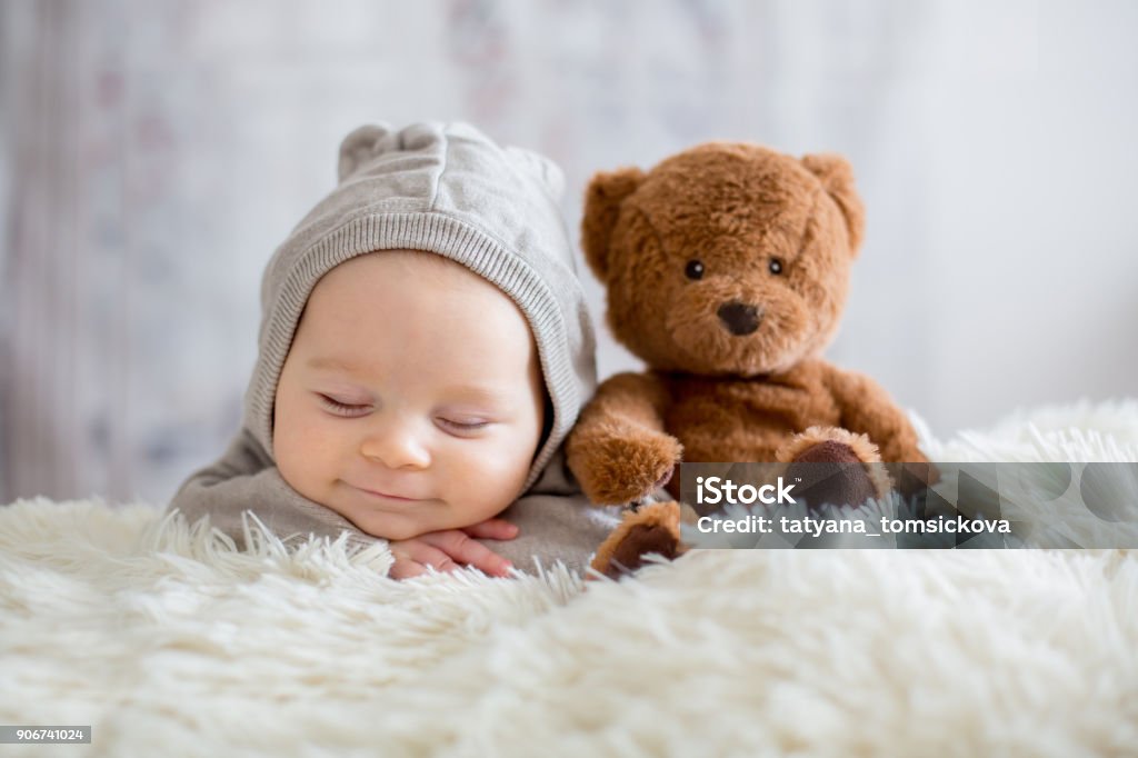 Sweet baby boy in bear overall, sleeping in bed with teddy bear Sweet baby boy in bear overall, sleeping in bed with teddy bear stuffed toys, winter landscape behind him Baby - Human Age Stock Photo