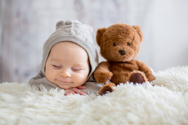 Sweet baby boy in bear overall, sleeping in bed with teddy bear Sweet baby boy in bear overall, sleeping in bed with teddy bear stuffed toys, winter landscape behind him group of babies stock pictures, royalty-free photos & images