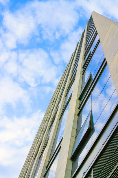 istock Looking up at skyscrapers with glass windows under blue sky and white clouds 906751972