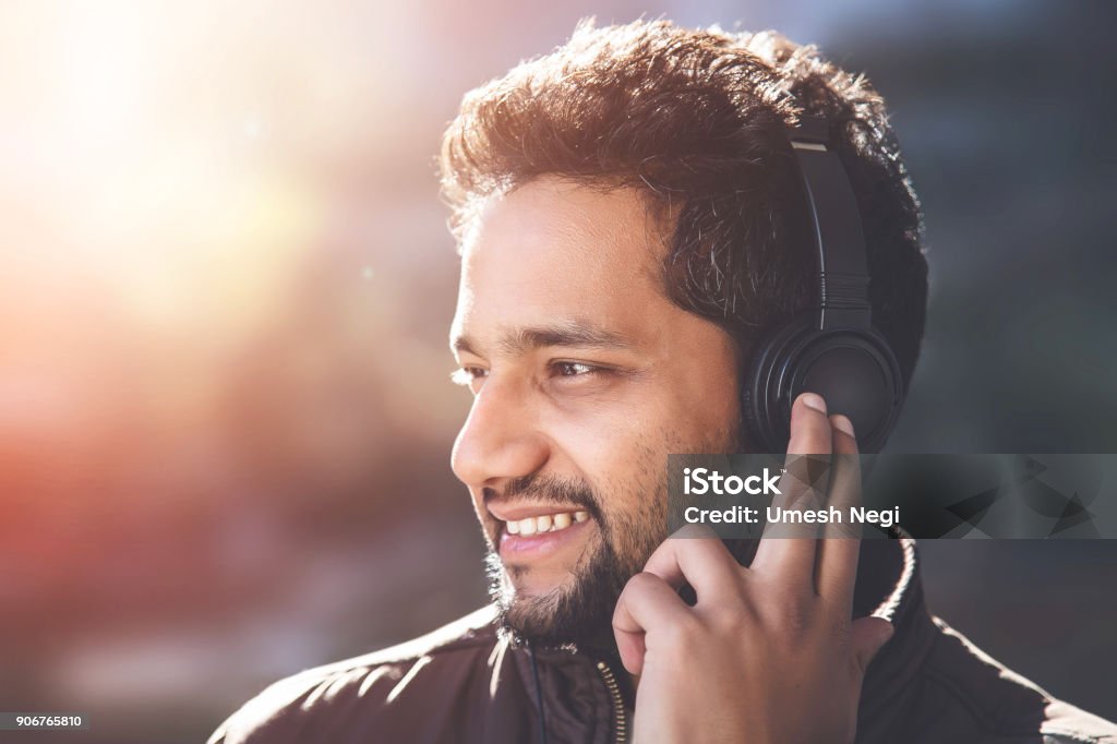 Young Asian/Indian man listening to music Close-up portrait of Young Indian Asian man listening to music with headphones, outdoors background 30-34 Years Stock Photo