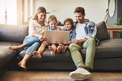 Shot of a mother and father using a laptop with their son and daughter on the sofa at home