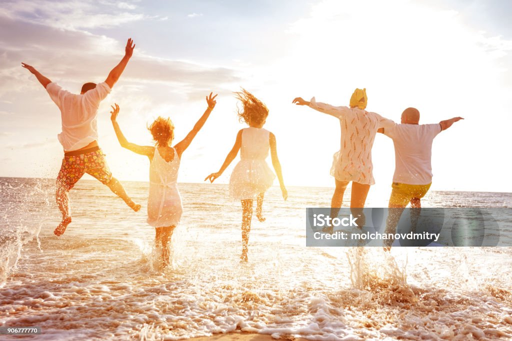 Group of five peoples run and jump to sunset sea Group of five happy peoples run and jump to sea beach against sunset sun Family Stock Photo