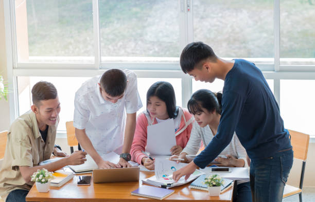 istock Asian College groups of students using laptop, tablet, studying together with notebooks documents paper for report near windows in classroom. Happy young study for school assignment, Soft focus 906782912