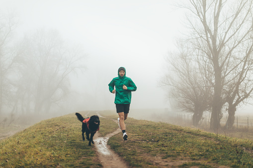 Photo of active young man jogging with his dog in a foggy morning