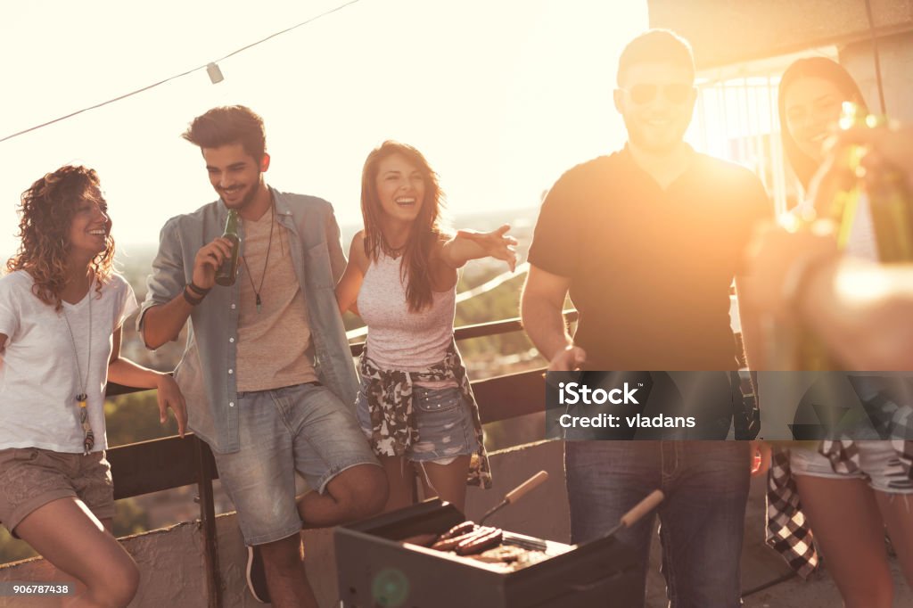 Bringing more beer Young friends making barbecue, drinking beer and enjoying hot summer days having fun on a rooftop party. Focus on the girl in the middle Barbecue Grill Stock Photo