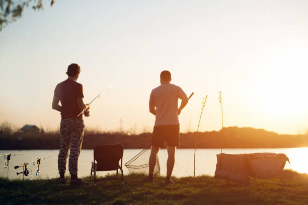 jeune homme pêche sur le lac au passe-temps de profiter du coucher du soleil - wading vertical water sport recreational pursuit photos et images de collection