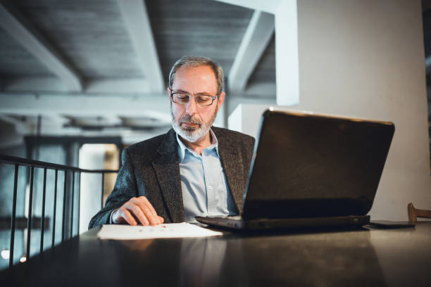 istock Co-Working Space in High-End Restaurants. Senior businessman with beard working on laptop in restaurant. 906824632