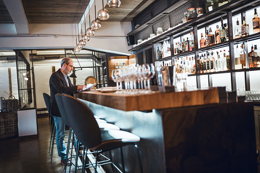 Mature businessman working at the bar in high end restaurant. He is using digital tablet