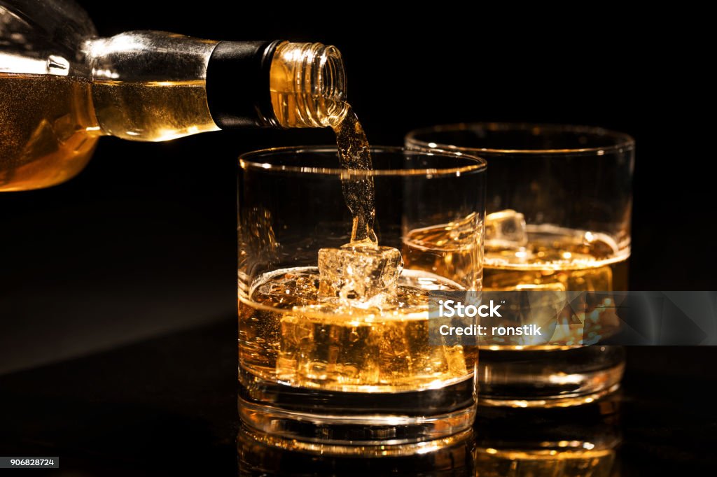 verser le whisky dans un verre avec des glaçons sur fond noir - Photo de Whisky libre de droits