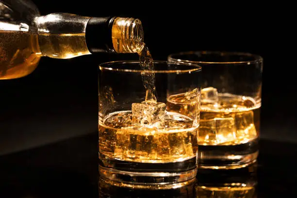 pouring whiskey into a glass with ice cubes on black background