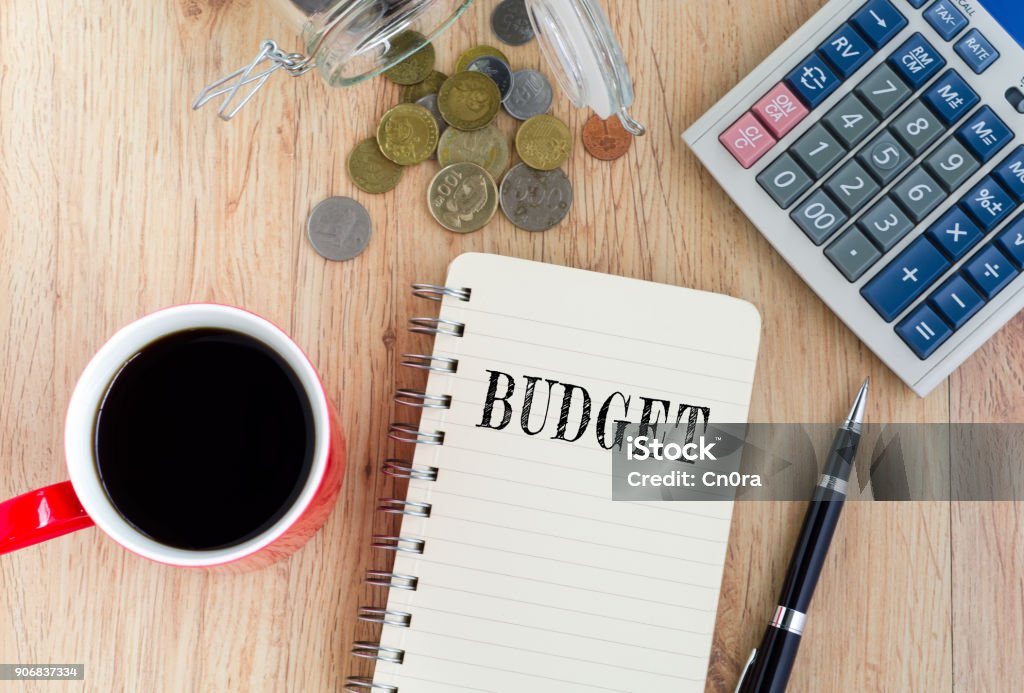 BudgetText on Notepad Budget text on notepad - coffee, coins,pen and calculator on top of wooden table. Home Finances Stock Photo