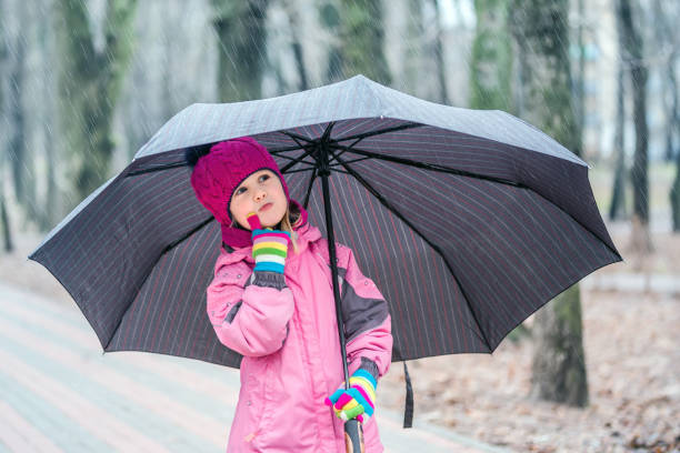 Beautiful young teenage girl of Indian ethnicity standing outdoors and holding multicolor umbrella in her hand and she checking rain.